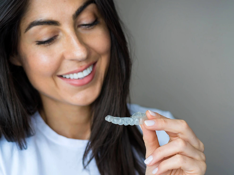 woman holding clear aligner tray, adult orthodontic treatment, subtle teeth straightening