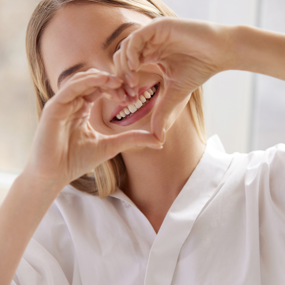A woman with a warm, healthy smile holds her hands to her heart gratefully.