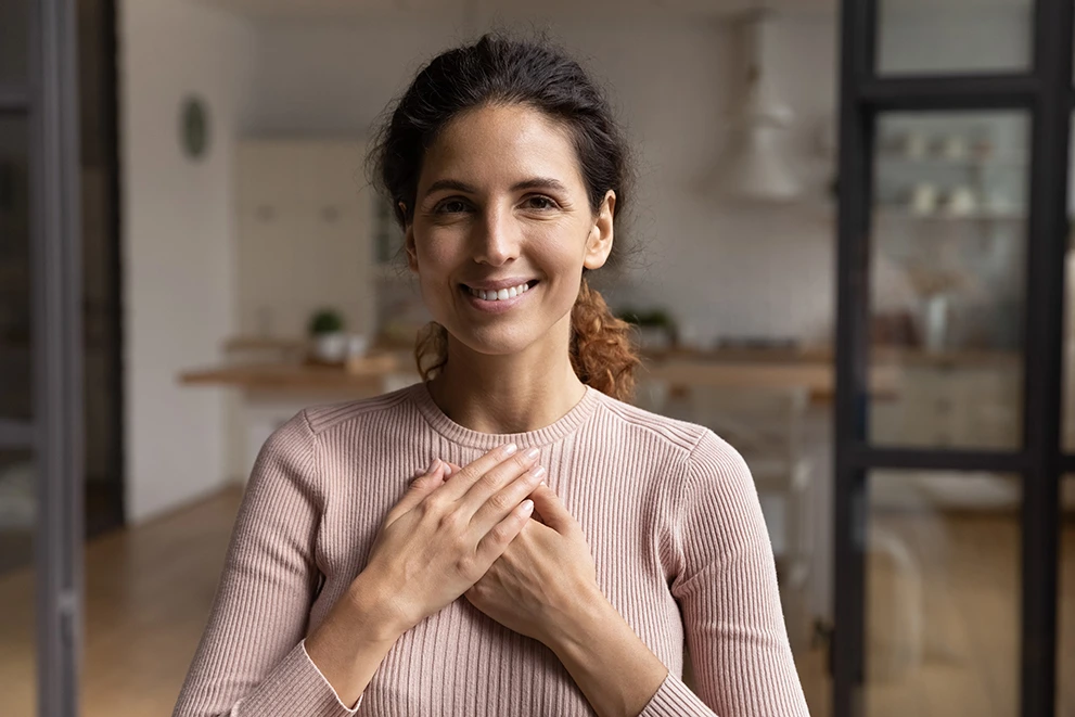 A woman with a warm, healthy smile holds her hands to her heart gratefully.
